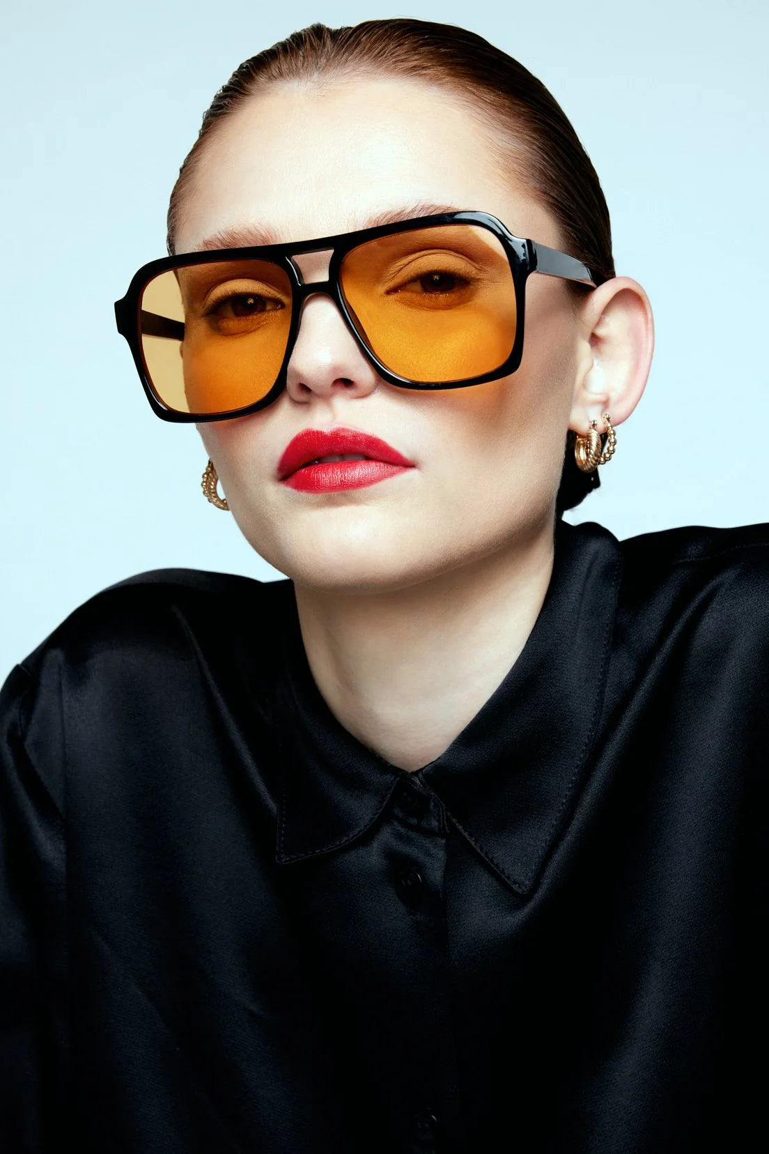 Editorial portrait in orange-tinted sunglasses and a black shirt