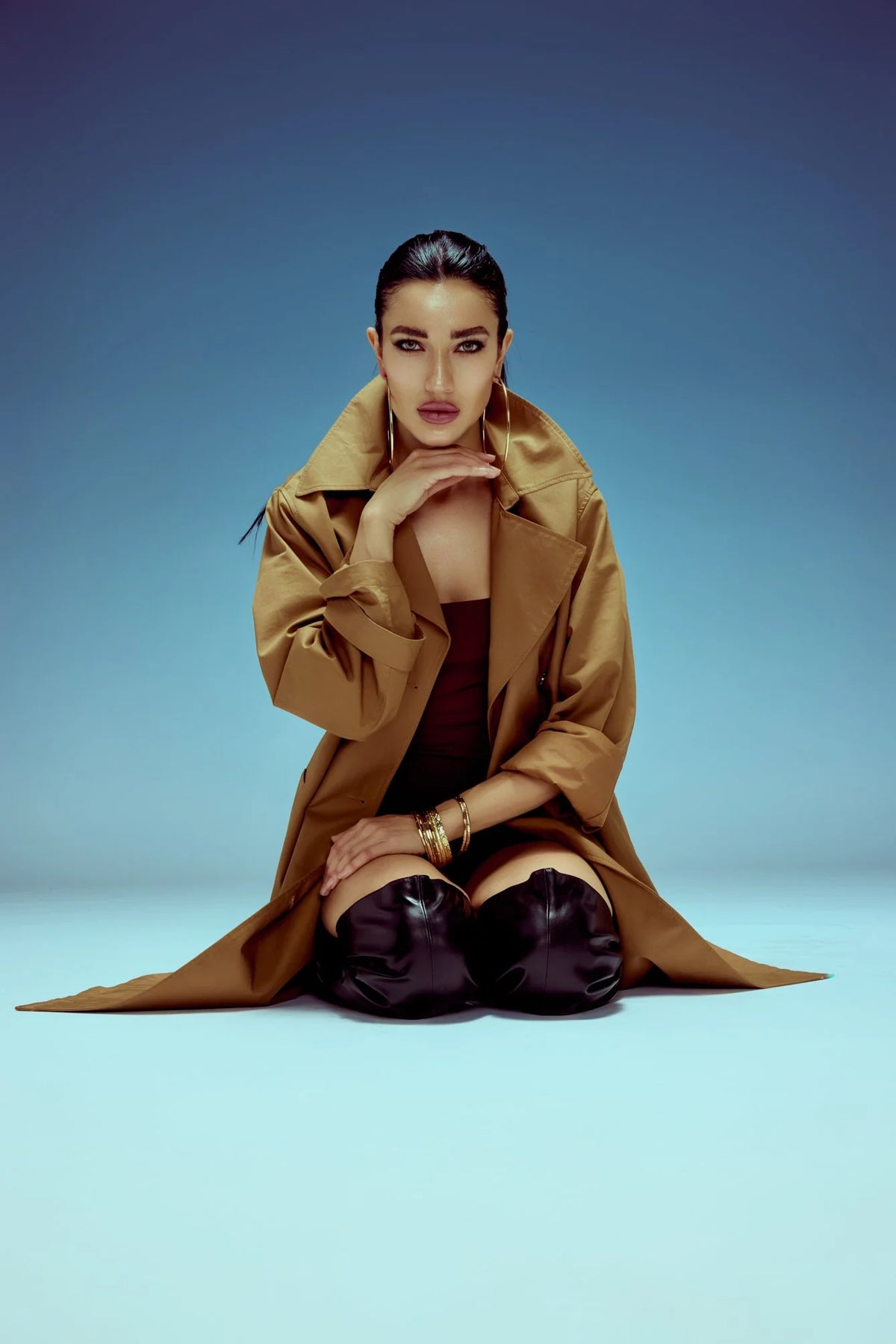 Camel coat, crouched pose on a soft blue backdrop