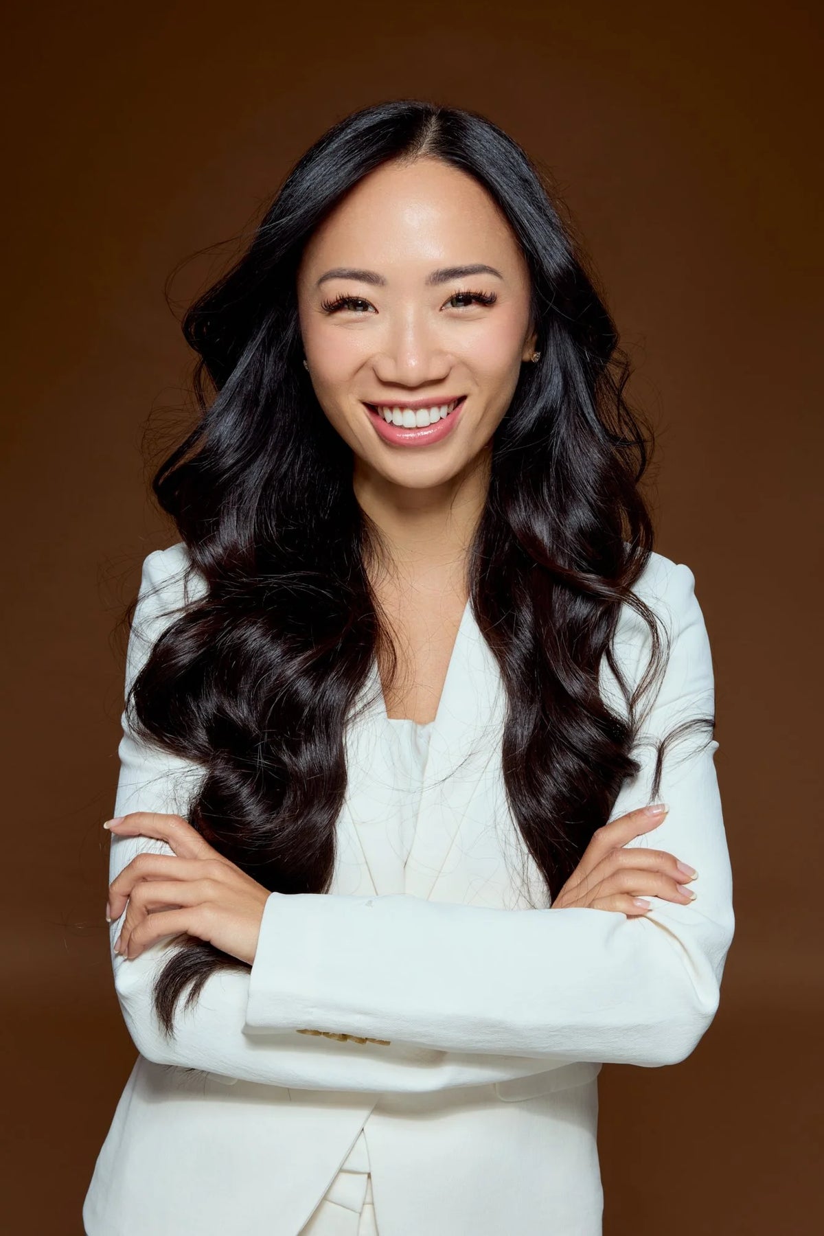 Corporate headshot of a woman in a white blazer, arms crossed, smiling