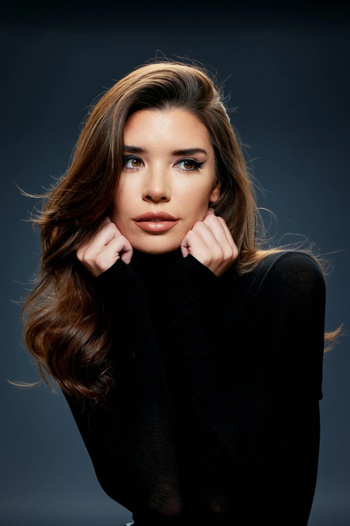 Woman in a black turtleneck, hands at her face, warm studio light