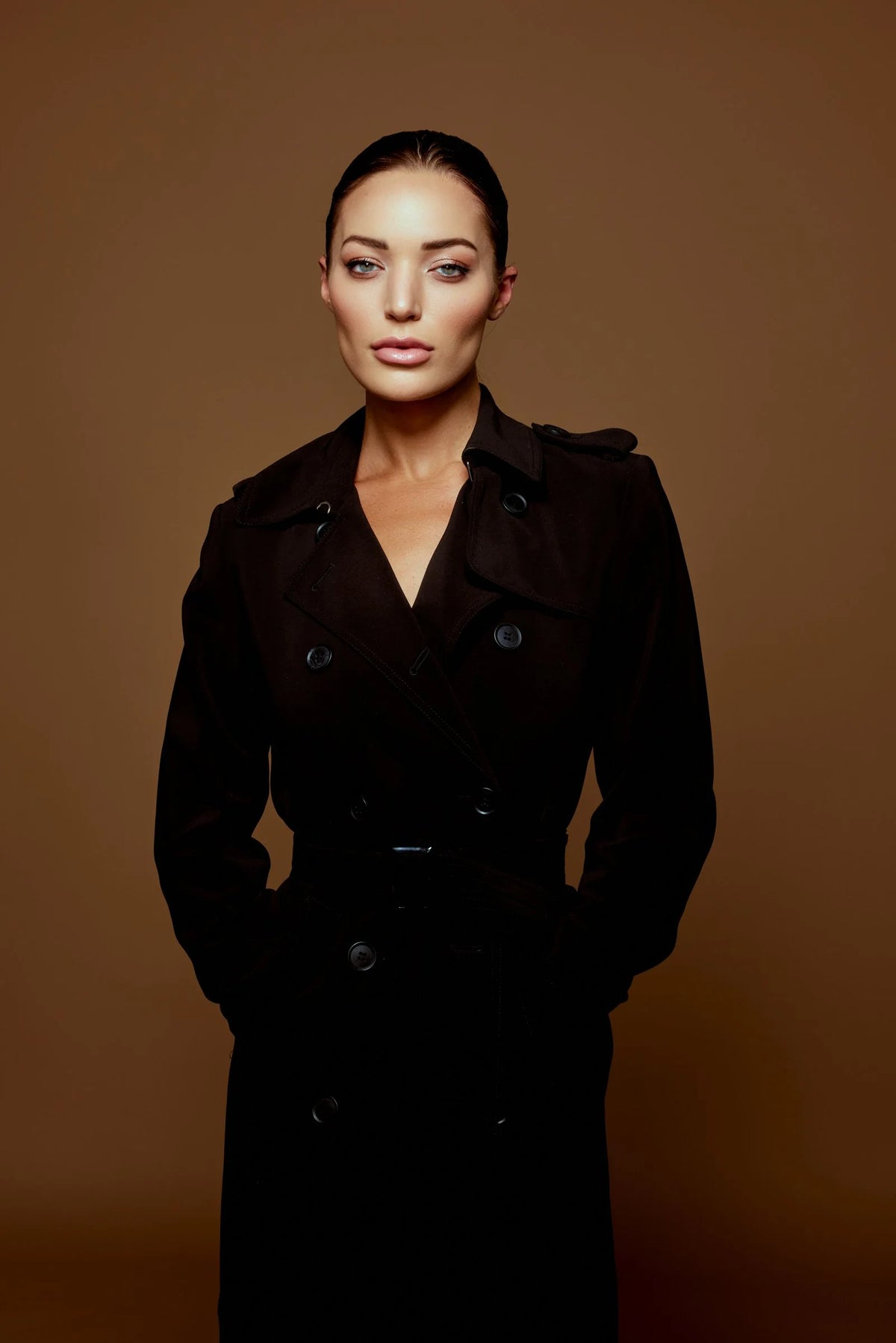 Woman in a long black coat on a warm brown backdrop