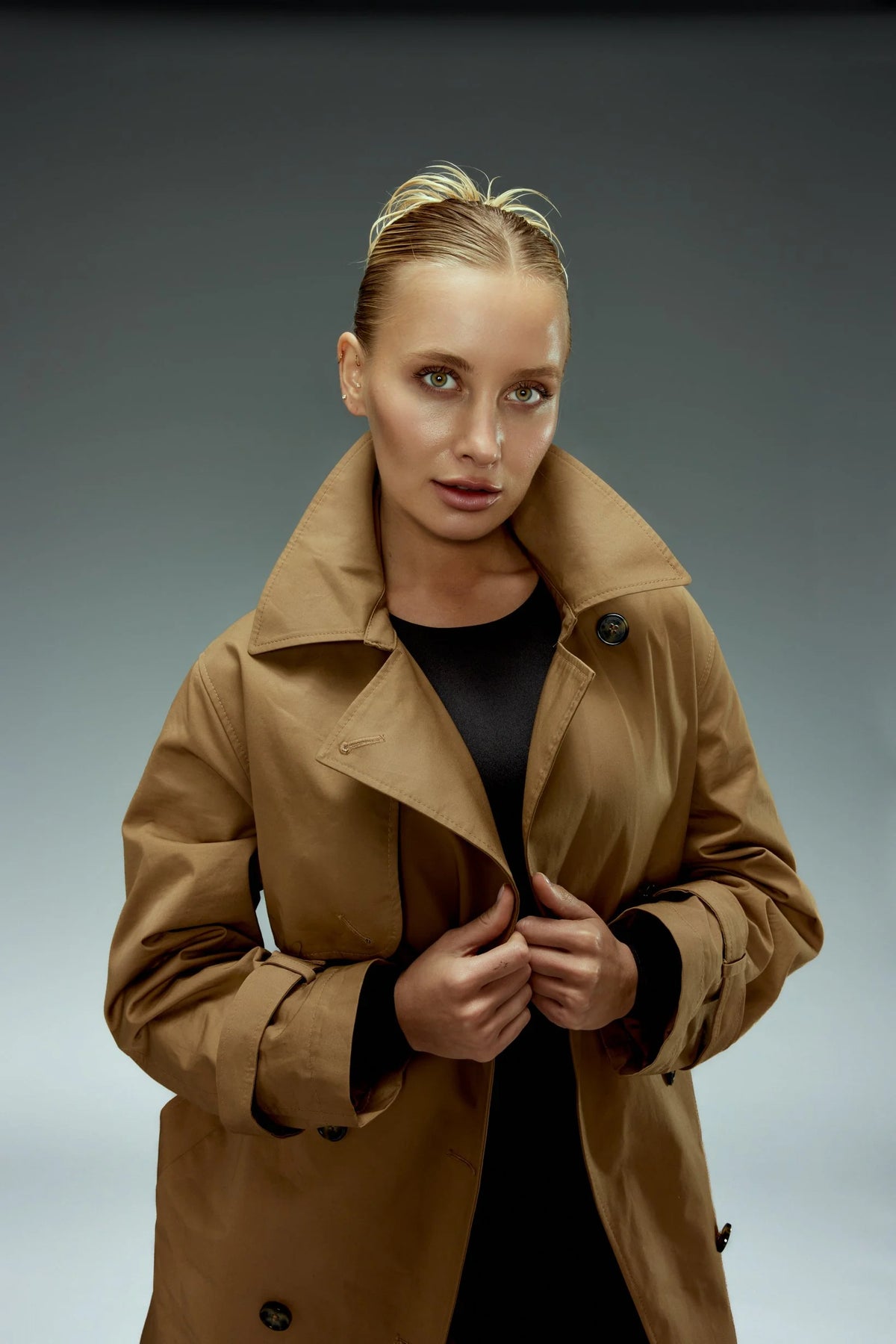 Woman in a camel trench coat on a slate backdrop