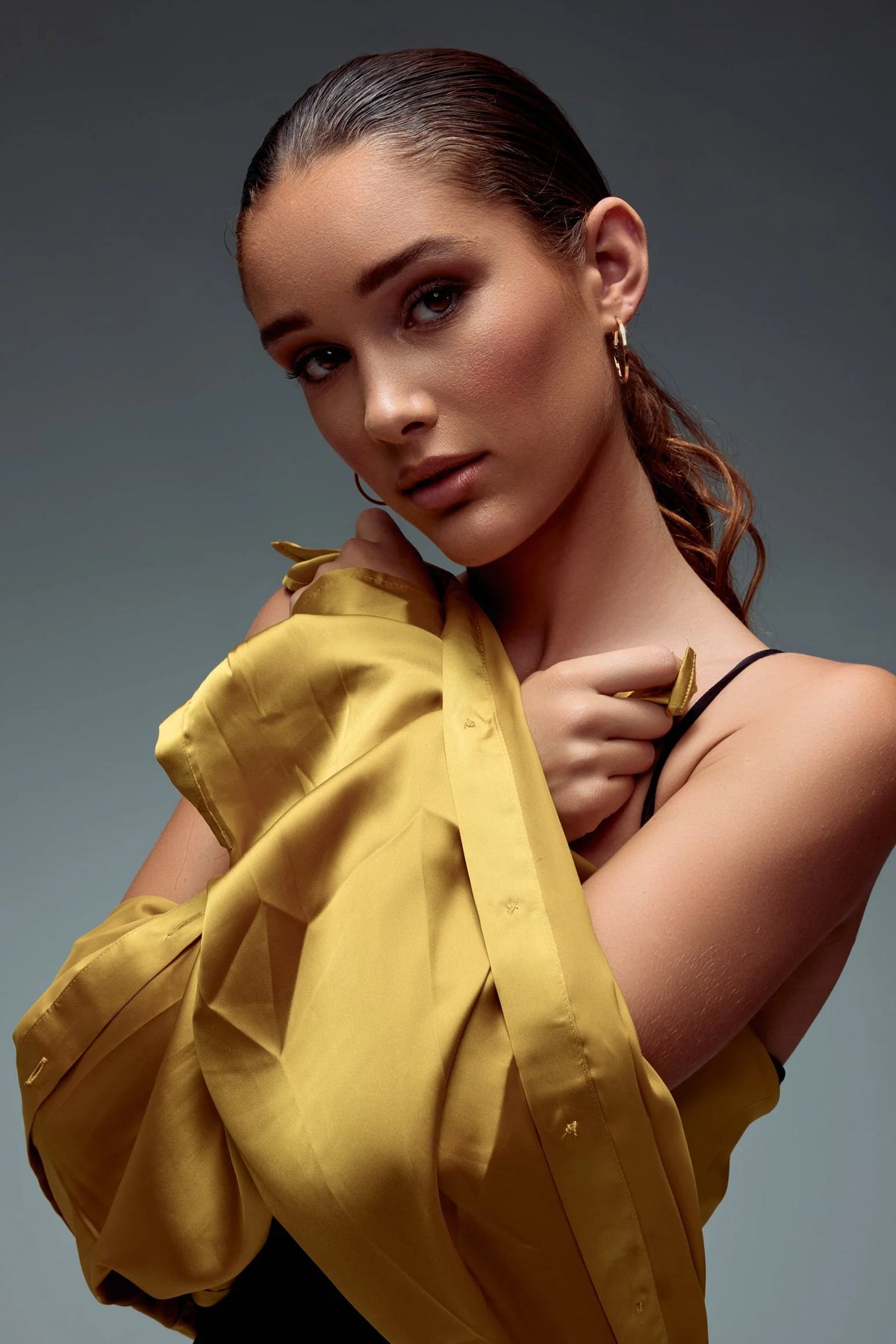 Woman in a gold satin top, hand at her collar